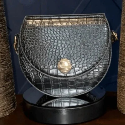 Black crocodile embossed leather crossbody bag with gold clasp on display