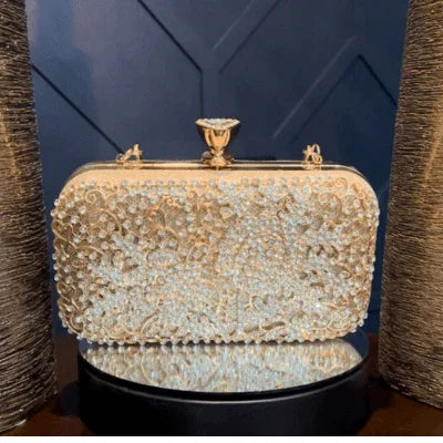 Gold beaded clutch purse with ornate floral design on a reflective surface, elegant evening bag