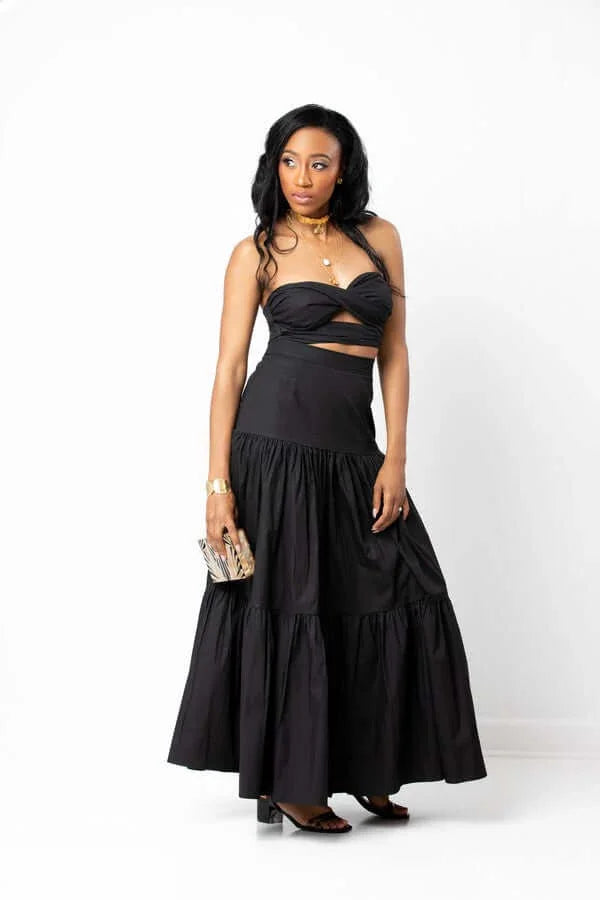 Woman in black two-piece maxi skirt set with clutch, posing on white background