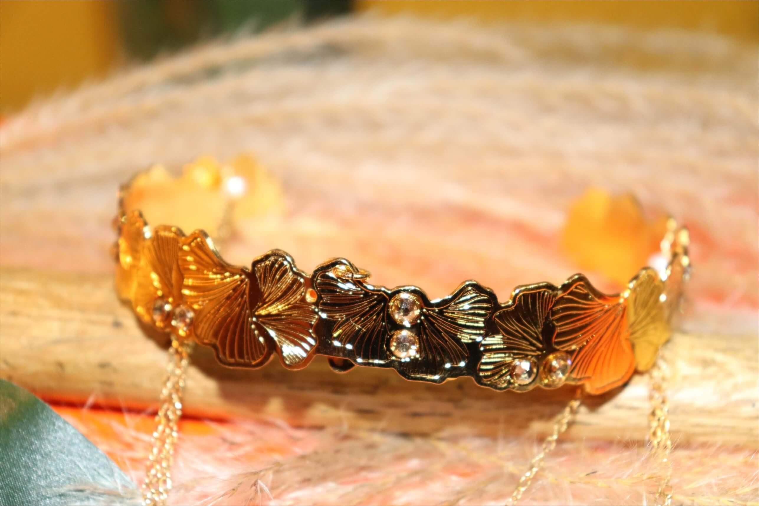 Gold floral bracelet with leaf designs and crystal accents on a natural wood background