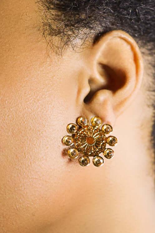 Gold floral stud earring with intricate pattern worn on ear