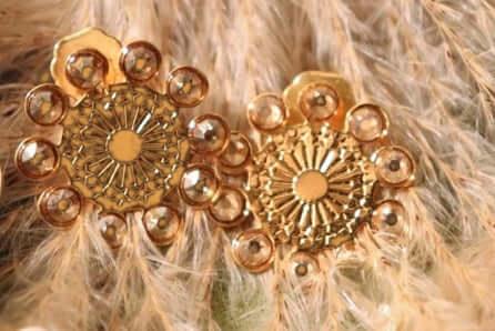Gold round stud earrings with intricate design on soft beige feather background