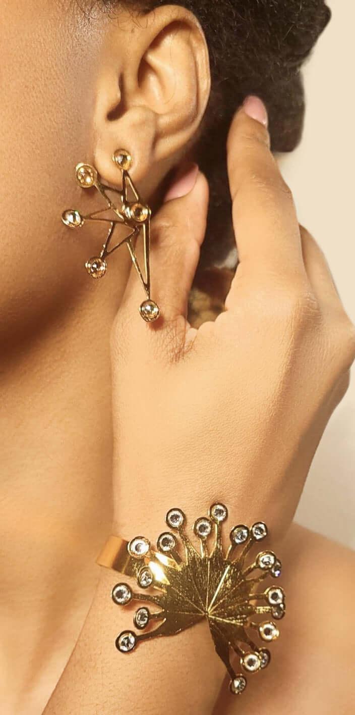Gold geometric statement earring and bracelet with crystal accents on woman's hand and ear