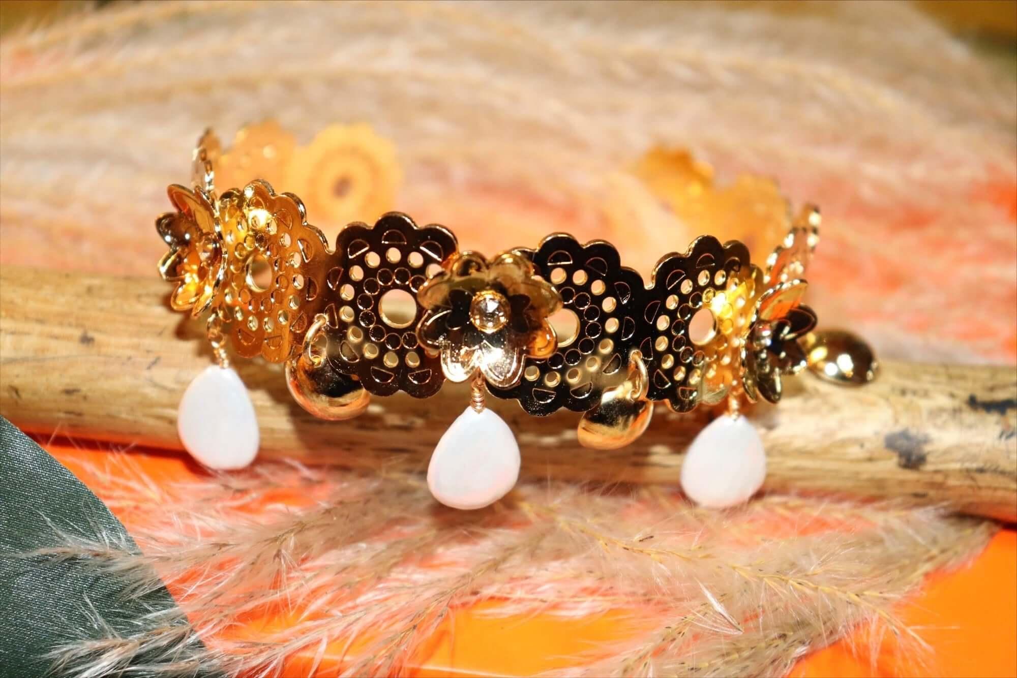 Gold floral bracelet with dangling white teardrop charms on rustic wood and orange background