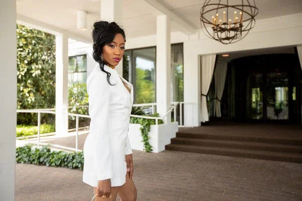 Woman in elegant white blazer dress standing outside upscale building entrance